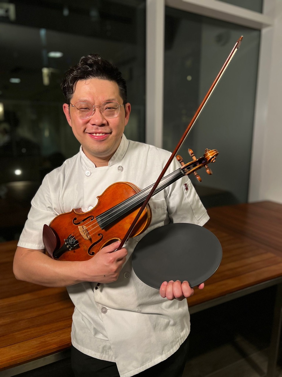 Nourvo founder Abraham Wong in a chef coat holding a violin and a plate in Vancouver